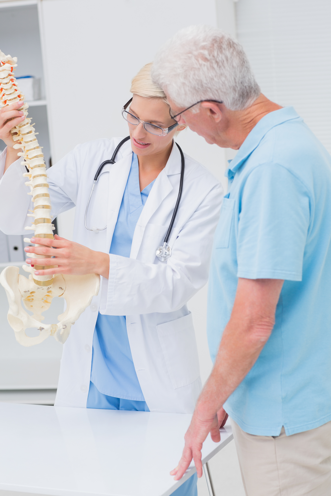 Female orthopedic doctor and senior patient discussing over anatomical spine in clinic